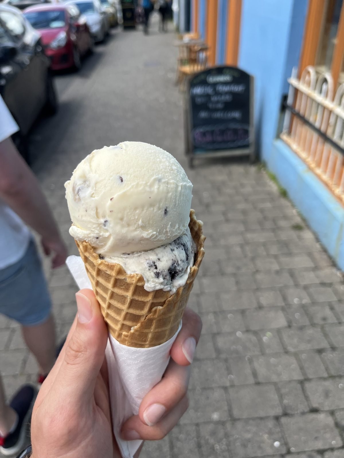 A waffle cone with a scoop, held up in the colourful Dingle street